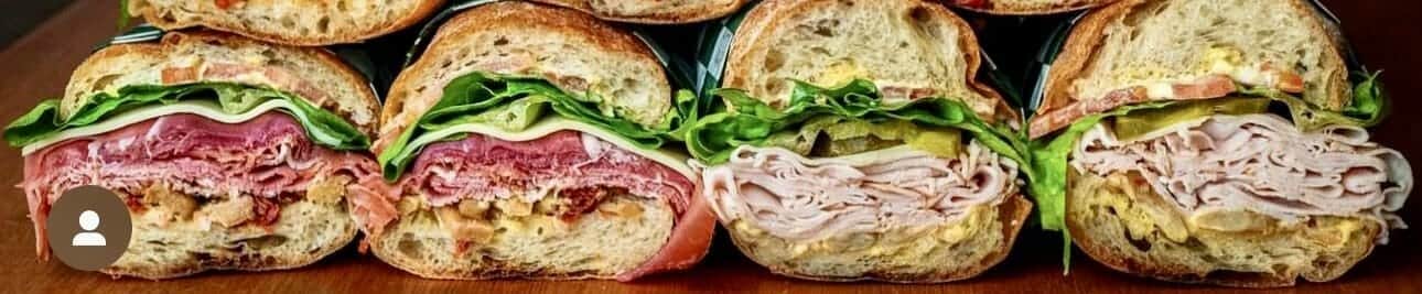 Stacked deli sandwich cut to show turkey, roast beef, and greens